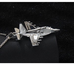 Detailed close-up of a silver fighter jet pendant on a black textured background