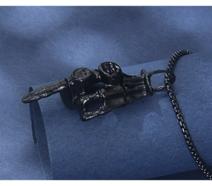 Macro shot of gothic black skeleton hand pendant with middle finger gesture on bead chain