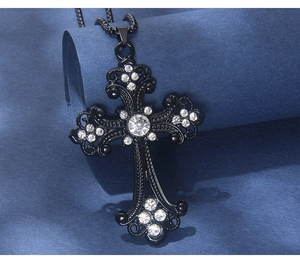 Dettaglio della collana con croce in acciaio nero e cristalli su uno sfondo blu scuro