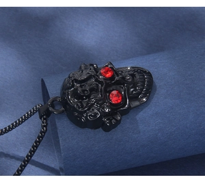 Détail d'un pendentif crâne gothique noir avec yeux en cristal rouge et chaîne métal