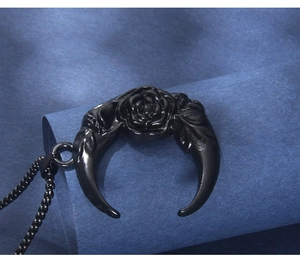Close-up of black crescent moon pendant with rose engraving on blue textured background
