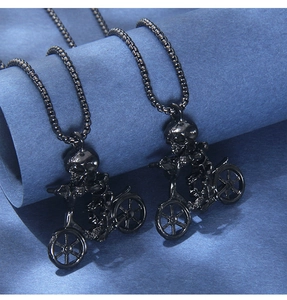 Close-up of a black skull riding a bicycle pendant with matching box chains on dark background