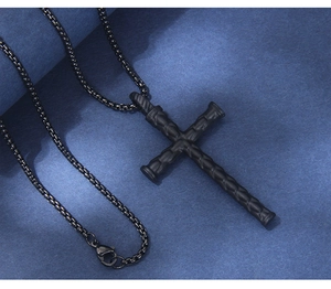 Detailed close-up of matte black nail-style cross pendant on dark textured background