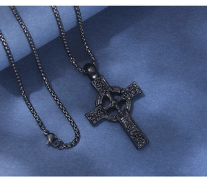 Détail macro d'un collier croix celtique noire avec des motifs en relief sur fond bleu