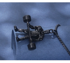 Vue macro d'un pendentif haltérophile noir et sa chaîne à maillons sur tissu bleu