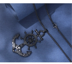 Macro shot of black stainless steel nautical anchor and ship wheel pendant on a textured base