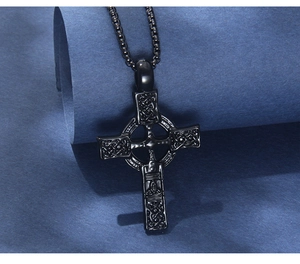 Détail d'un pendentif croix celtique noire avec motifs de nœuds sur une chaîne à billes