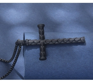Detailed macro view of black stainless steel cross pendant with textured woven pattern detail