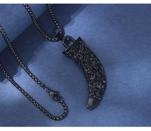 Detail of black wolf tooth pendant with ornate floral engraving on a steel box chain