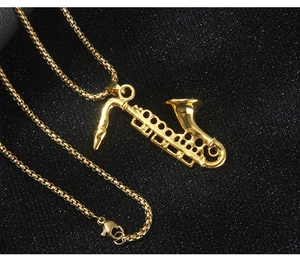 Close-up of golden saxophone pendant with detailed keys and round box chain on black texture