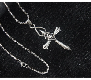Détail macro du pendentif croix vintage en argent avec chaîne gourmette sur fond noir