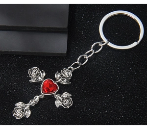 Macro detail of silver gothic cross keychain with red heart gemstone and roses
