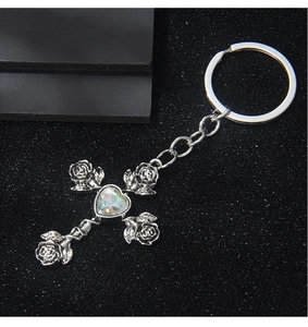 Macro view of silver cross keychain with rose details and iridescent heart stone