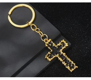 Detail view of gold-plated cross keychain with black enamel inlay and textured wavy edges