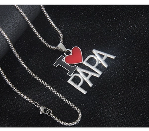Détail macro du collier argenté MOM PAPA avec pendentif cœur rouge sur fond noir