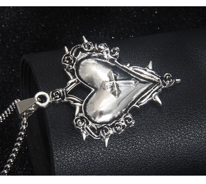 Détail d'un pendentif cœur gothique argenté avec épines et roses sur cuir noir élégant