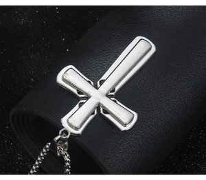Makroaufnahme von Silber-Kreuzanhänger mit weißem Emaille auf schwarzem Leder