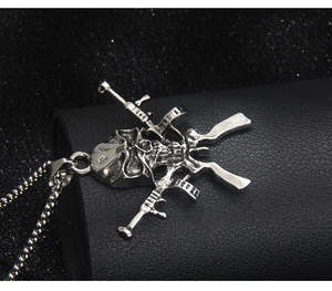 Vue détaillée du pendentif crâne punk avec deux mitrailleuses croisées sur chaîne à billes