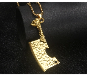Close-up of golden cleaver pendant with skull handle on black leather texture