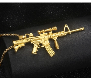 Detail of golden assault rifle pendant with scope and box chain on black texture