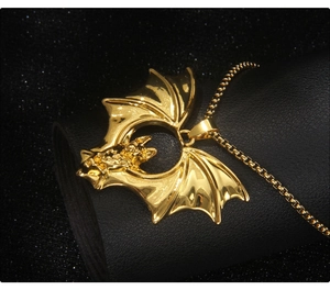 Close-up of golden bat wing pendant with devil motif on black textured background