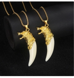 Detail of two gold wolf head necklaces with ivory fangs on black textured leather surface