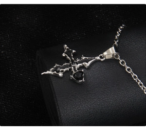 Close-up of gothic stainless steel cross necklace with black enamel heart and spikes