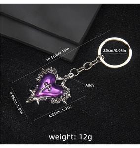 Macro detail of Gothic heart keychain with silver cross and thorn pattern on black fabric