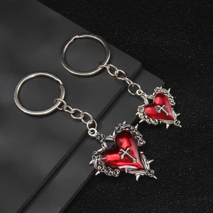 Gothic red heart cross keychain with thorn details and silver ring on dark background