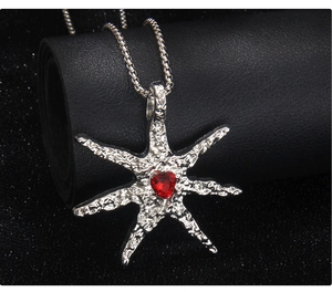 Detail of silver starfish pendant with red heart gemstone and hammered metal texture