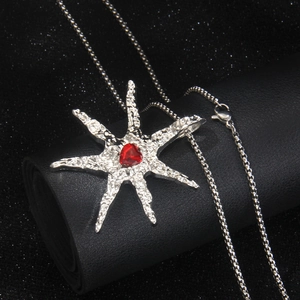 Silver-toned starfish necklace with a red heart gemstone on a dark textured surface