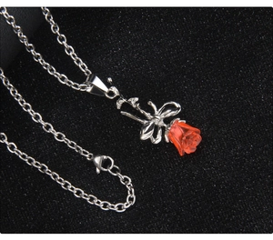 Détail macro du collier rose argenté avec fleur en résine rouge et pendentif nœud