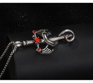 Vue macro d'un pendentif épée dragon argenté avec strass rouges et chaîne à billes