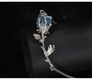 Detalle del collar de rosa con hojas plateadas y cristal azul en forma de pera