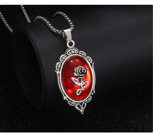 Macro detail of gothic rose pendant with red oval gem and ornate silver scrollwork