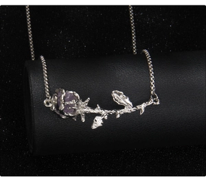 Detalle del collar de rama de rosa plateada con gema púrpura en exhibidor negro