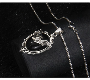 Close-up of gothic silver bat necklace with an oval black stone on a dark textured surface