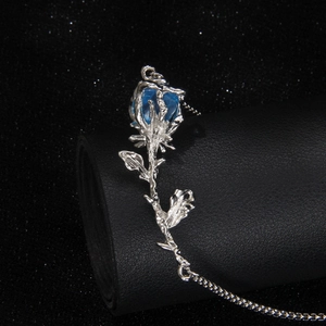 Collar de rosa 3D plateada con gema azul sobre fondo negro de cielo estrellado