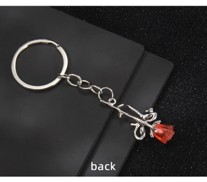Detailed back view of red rose keychain with silver chain and leaf on dark surface