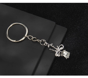 Detail showing a silver rose keychain with bow accent on a black textured surface