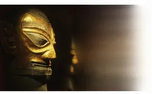 Dettaglio del ciondolo a maschera Sanxingdui con finitura in bronzo e oro