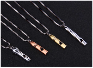 Détail de quatre pendentifs sifflets en argent, cuivre et bronze sur fond noir mat