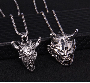 Close-up of punk silver sheep skull and Hannya mask pendants on black leather texture