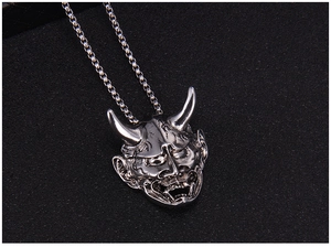 Macro detail of silver Hannya demon mask pendant with intricate fangs and dark textures