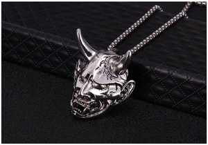 Detailed close-up of antique silver Hannya mask pendant with sharp horns and demon fangs