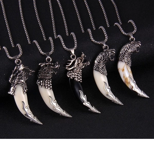 Detail of vintage wolf tooth pendants featuring dragon and tiger metal carvings on black background