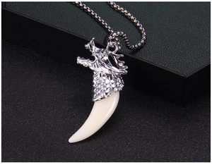 Gros plan sur un pendentif tête de dragon en acier avec dent de loup sur fond texturé
