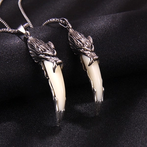 Vintage dragon head pendant with white curved tusk on black silk background