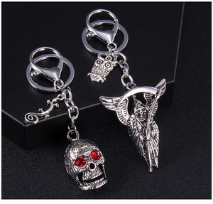 Macro detail of punk skull and grim reaper keychains with red gemstone eyes on black stand