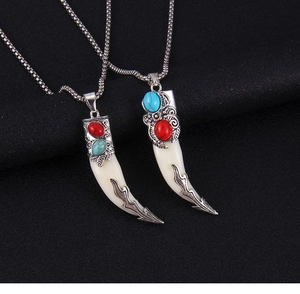 Détail de pendentifs dent de loup tribaux avec gravures et gemmes rouges et bleues